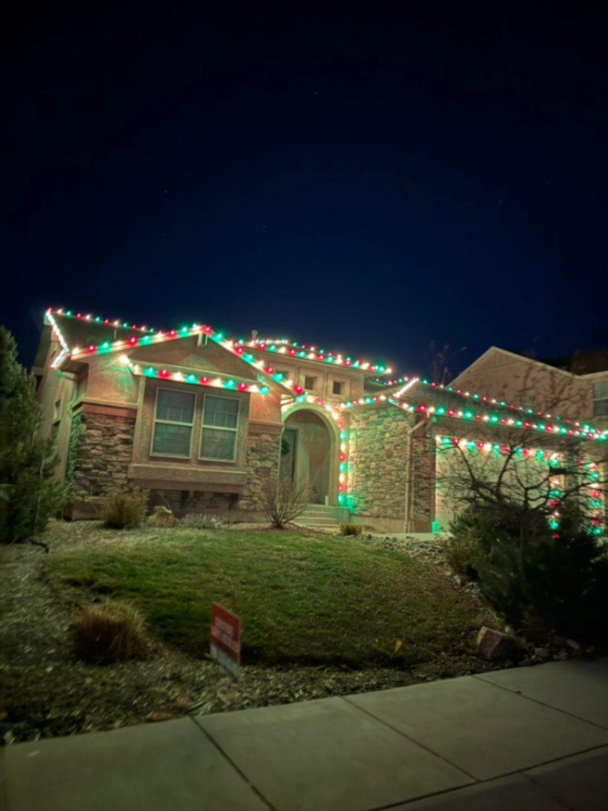 Holiday light installation Colorado Springs CO - stunning Christmas lights on two-story home with multicolor LED bulbs, professional roofline lighting and landscape illumination